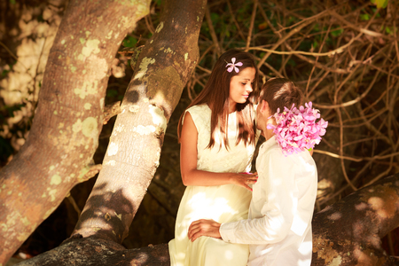 brunette bride in long white wedding dress sitting on the big tree and hold her handsome groom on island beach in Thailandの写真素材