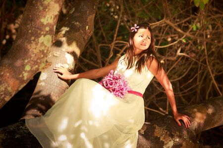 brunette bride in long white wedding dress and bridal bouquet sitting on the big tree on island beach in Thailandの写真素材