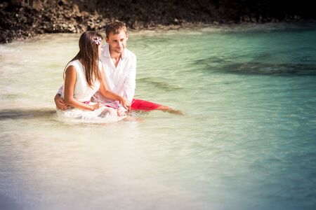 brunette girl with handsome man sitting in sea water in island bay with green mountain backgroundの写真素材