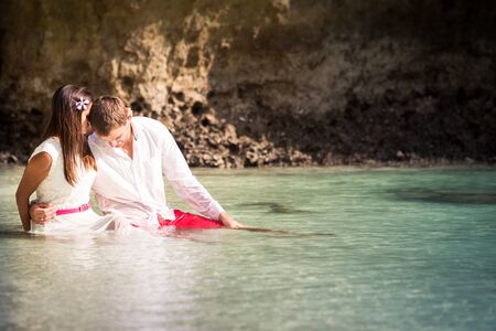 brunette girl with handsome man sitting in sea water in island bay with green mountain backgroundの写真素材