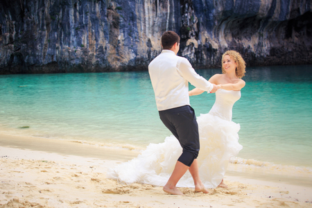 handsome groom twist his blonde bride in elegant wedding dress near cliff on island beach Thailandの写真素材