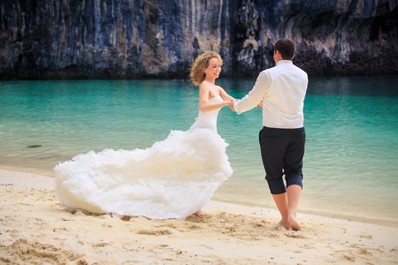 handsome groom twist his blonde bride in elegant wedding dress near cliff on island beach Thailandの写真素材