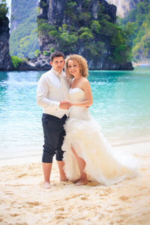 handsome groom with his blonde bride in elegant wedding dress pose near cliff on island beach Thailandの写真素材