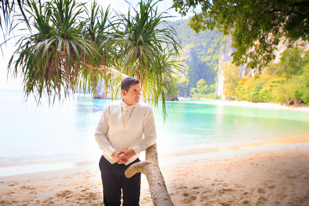handsome groom in white shirt stand near palm tree on island beach Thailandの写真素材