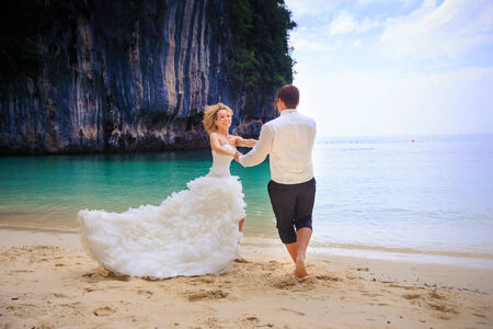 handsome groom twist his blonde bride in elegant wedding dress near cliff on island beach Thailandの写真素材