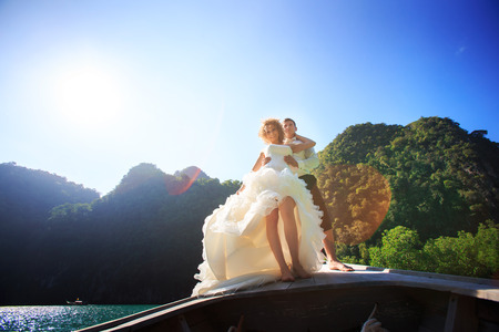 blonde bride and handsome groom stand on longtail boat in Thailandの写真素材