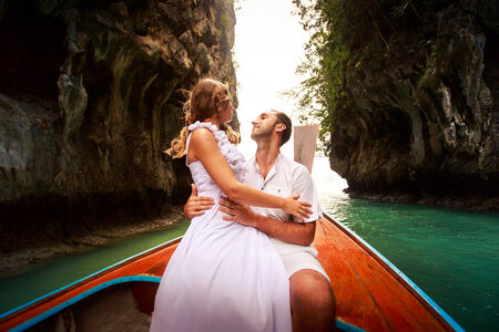 blonde bride sits on handsome groom knees sitting on longtail boat against cliff islandの写真素材