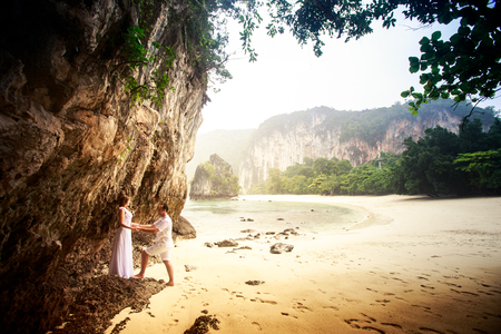 bride and groom hold together hand in hand on sand beach near cliff against sea rocks treesの写真素材