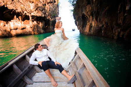 blonde bride and handsome groom sit on longtail boat in Thailandの写真素材