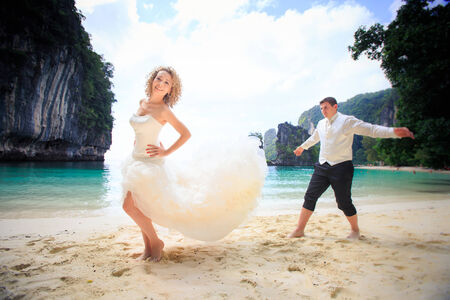 handsome groom with his blonde bride in elegant wedding dress pose near cliff on island beach Thailandの写真素材
