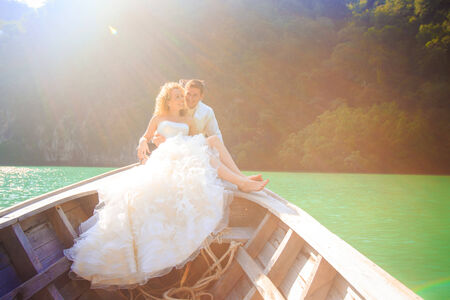 blonde bride and handsome groom sit on longtail boat in Thailandの写真素材