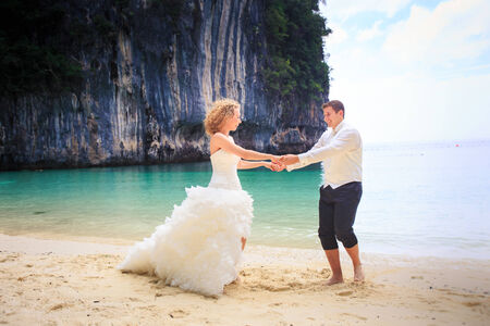 handsome groom twist his blonde bride in elegant wedding dress near cliff on island beach Thailandの写真素材
