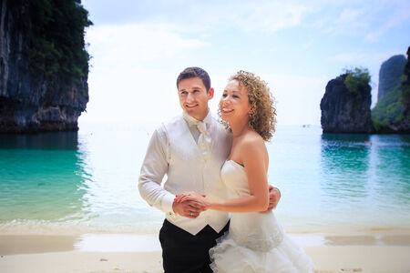 handsome groom with his blonde bride in elegant wedding dress pose near cliff on island beach Thailandの写真素材