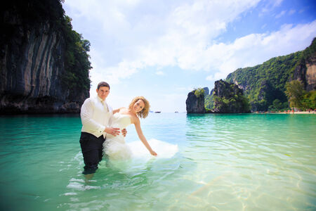blonde bride in elegant wedding dress and handsome groom pose standing in sea water in Thailandの写真素材