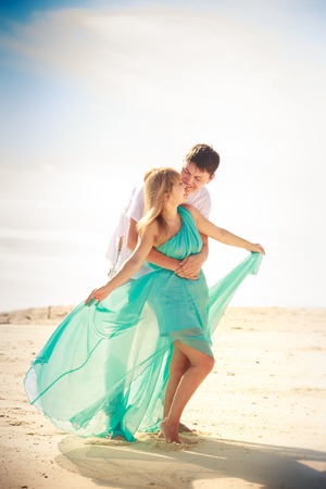 handsome man hold his beautiful blonde wife in elegant dress on island beachの写真素材