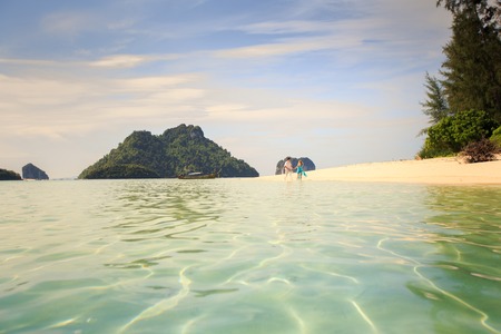 handsome man run with his beautiful blonde wife in elegant dress on island beach with green mountain on backgroundの写真素材