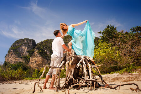 handsome man look at beautiful blonde woman in blue dress among green treesの写真素材