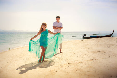 handsome man hold his beautiful blonde wife in elegant dress on island beachの写真素材