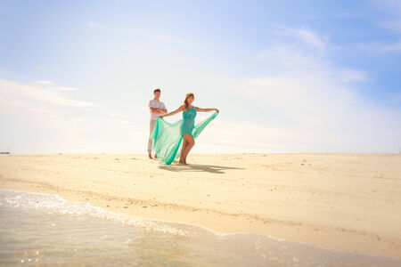 handsome man hold his beautiful blonde wife in elegant dress on island beachの写真素材