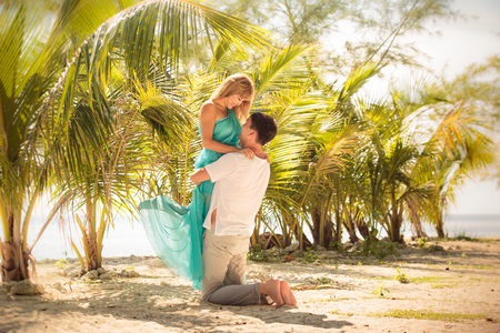 beautiful blonde woman in elegant dress kiss her handsome husband stand in green palm leafsの写真素材