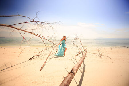 beautiful blonde woman in elegant dress pose near old trees near the blue oceanの写真素材