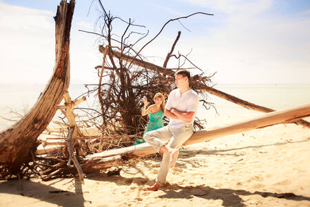beautiful blonde woman in elegant dress hold her handsome husband near old trees on islandの写真素材