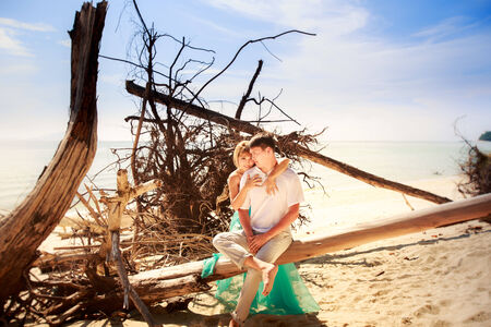 beautiful blonde woman in elegant dress hold her handsome husband near old trees on islandの写真素材