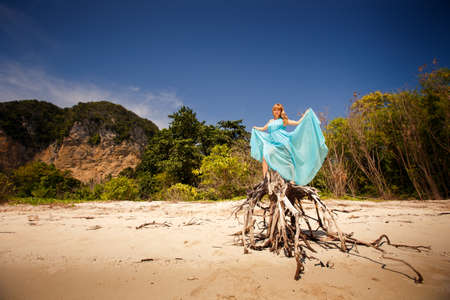 beautiful blonde woman play with her blue dress among green treesの写真素材