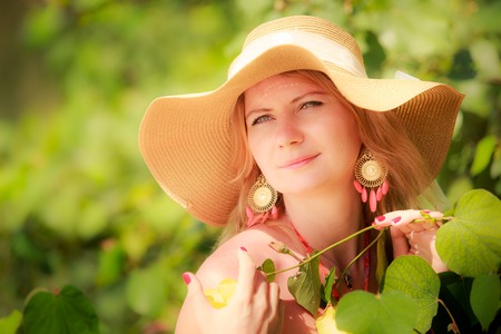 blonde longhaired blue eyed girl in straw hat poses with flowersの写真素材