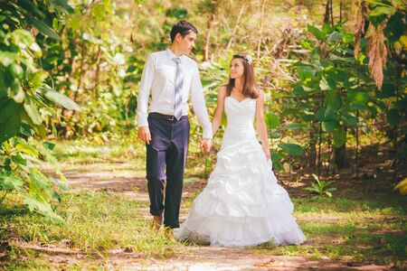 young brunette bride and groom walk hand in hand through green jungleの写真素材