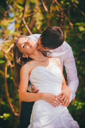 young brunette bride and handsome groom embrace in green jungleの写真素材