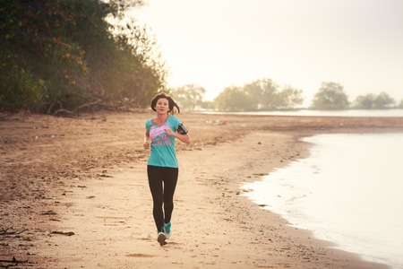 brunette girl in sports clothes runs on sand beach at low tide against sea at dawnの写真素材