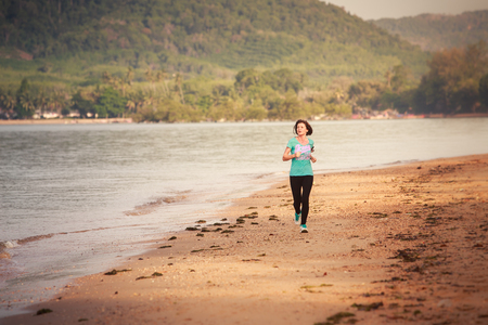 brunette girl in sports clothes runs from distance on sand beach at low tide against sea at dawnの写真素材