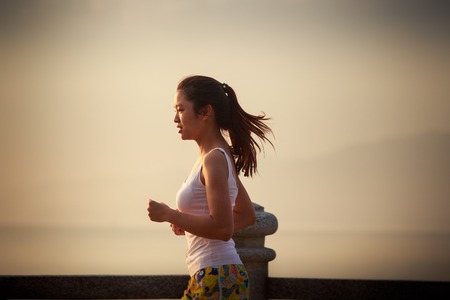 asian brunette girl in sports cloth runs on embankment against sea at sunriseの写真素材