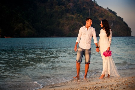 brunette bride and handsome groom barefoot walk at sand beach at dawnの写真素材