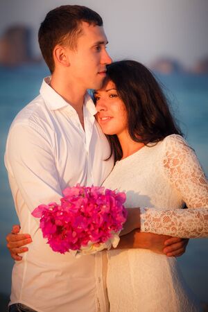 brunette bride and handsome groom barefoot stand at sand beach at dawnの写真素材