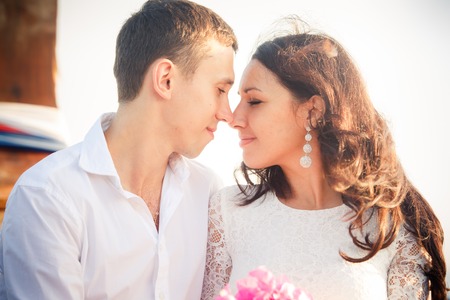 brunette bride and handsome groom look into eyes on longtail boat at sunriseの写真素材
