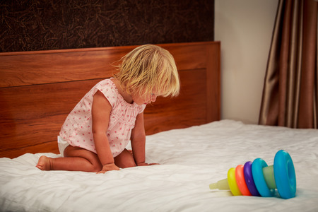 portrait of sitting on knees little blonde girl in pink dress near toy pyramid against brown wallの写真素材