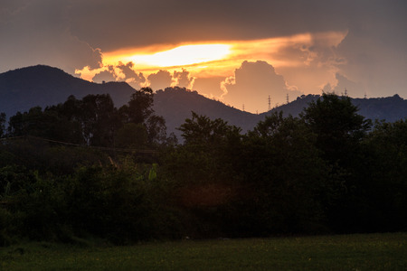 panorama of rising sunbeams from behind golden cumulus clouds in mountains with dark green plants on foregroundの写真素材