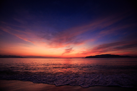 panorama of fantastic beautiful dark blue and red sky with fleecy clouds before sunrise and sea on foregroundの写真素材