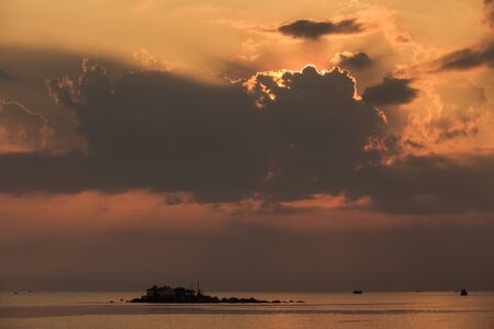 panorama of sunrise from behind golden cumulus clouds taken from embankment barrier against sea and islandの写真素材