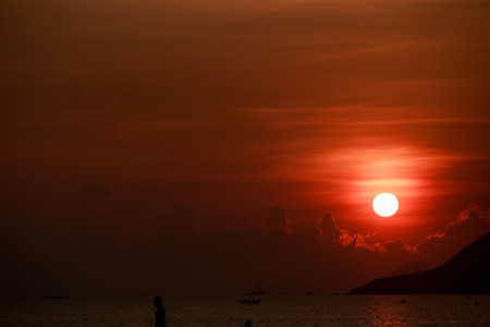 white disk of large sun among red sky above sea with sun path islands and fishing boats on horizon at sunriseの写真素材