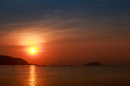 white disk of large sun among red sky above sea with sun path islands and fishing boats on horizon at sunriseの写真素材