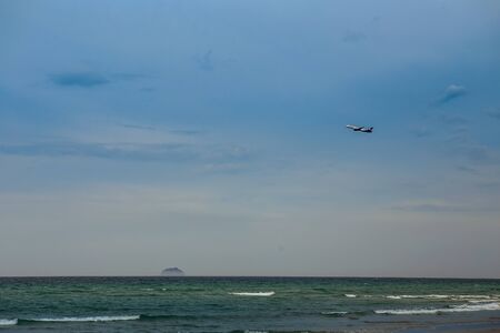 aircraft in blue sky above azure sea with foamy wavesの写真素材