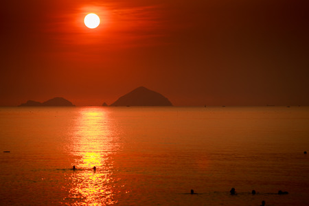 white disk of large sun among red sky above sea with sun path and islands at sunriseの写真素材