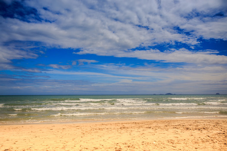 panorama of foamy wave surf on sand beach against blue sky and white cloudsの写真素材