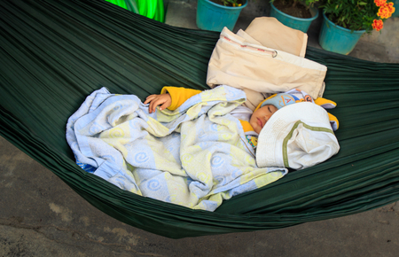 NHA TRANG, KHANH HOA / VIETNAM - FEBRUARY July 2016: Vietnamese baby covered with blue blanket sleeps in dark green hammock by flower pots on February 07 in Nha trangのeditorial素材