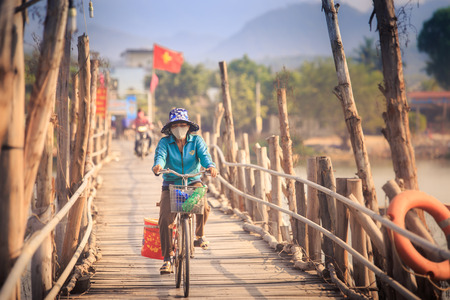 NHA TRANG, KHANH HOA/VIETNAM - JUNE 14 2016: Vietnamese woman rides a bicycle by the wooden bridge with vietnam flag on  background on June 14 in Nha Trangのeditorial素材