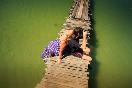 upper view guy photos blond girl leans on him sitting on old wooden pier against tropical azure seaの写真素材