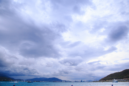 white grey clouds over dark blue sea distant resort city mountains boatsの写真素材